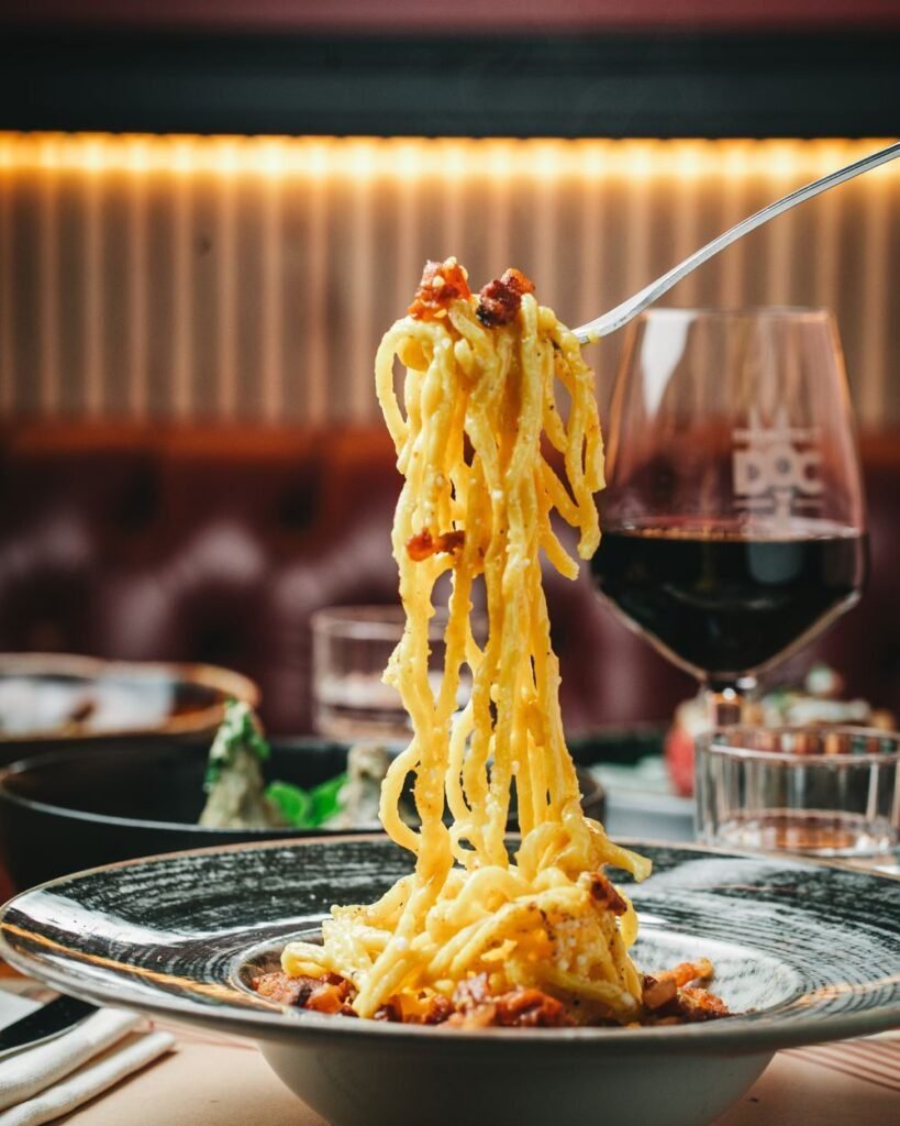Carbonara romana envuelta alrededor de un tenedor con una copa de vino