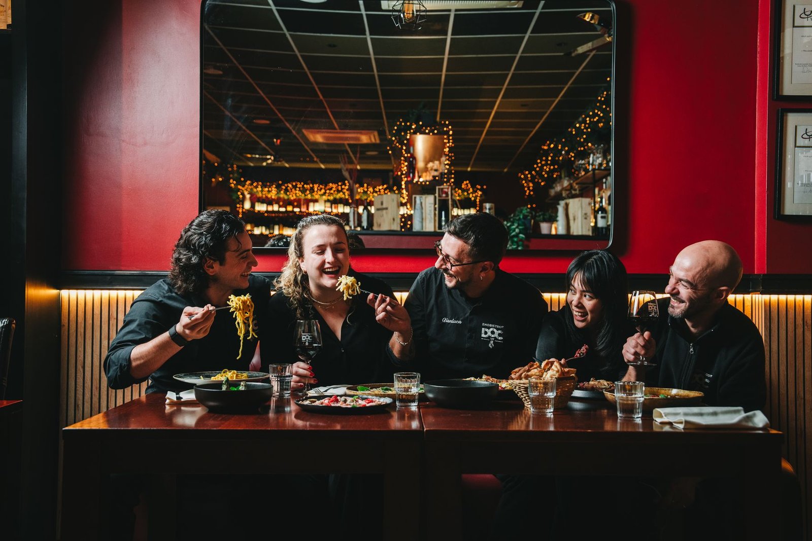 Сотрудники DOC EnoBistrot смеются вместе за столом перед домашними тарелками